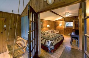 A wooden cabin bedroom with a bed, a desk, a swing, and a window. - The Normaway Inn (Margaree Valley)
