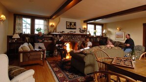 A cozy living room with a fireplace, wooden furniture, and a chessboard on the table. - The Normaway Inn (Margaree Valley)