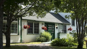 A white building with green trim and a green door, surrounded by trees and a gravel path. - The Normaway Inn (Margaree Valley)