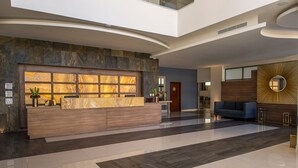 A modern lobby with a marble reception desk, a blue sofa, and a large mirror with a sunburst design. - Ocean View Beach Hotel (Mazatlán)