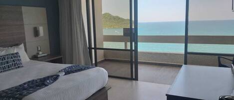 A bedroom with a large bed, a desk, and a view of the sea.