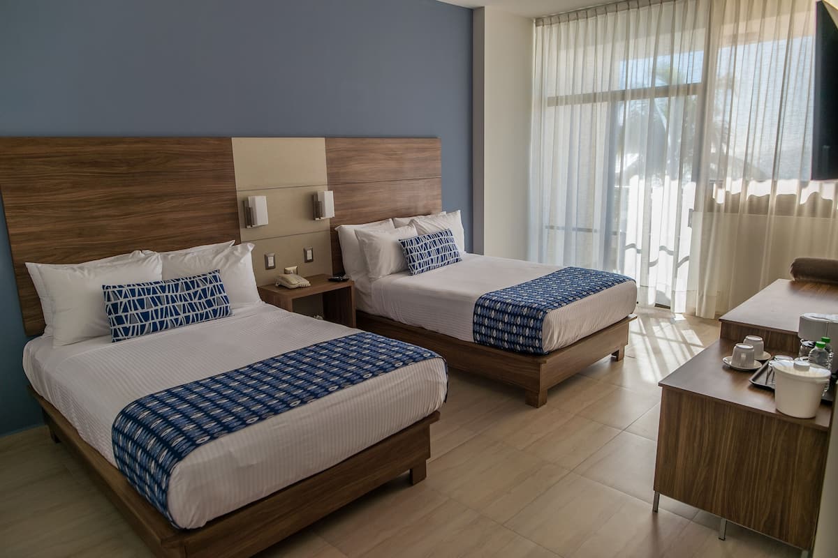 Habitación de hotel con dos camas, un escritorio y un ventanal con cortinas.