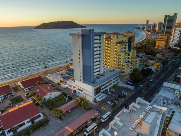 A coastal cityscape with high-rise buildings, a beach, and a small island in the distance.