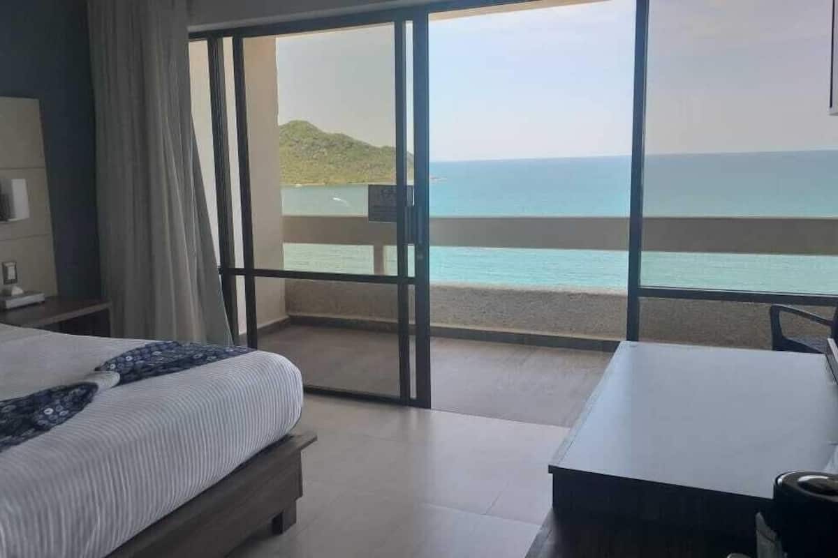 Un dormitorio con una cama grande, un escritorio y vista al mar.