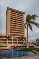Un hotel alto con varios pisos, piscina y palmeras.