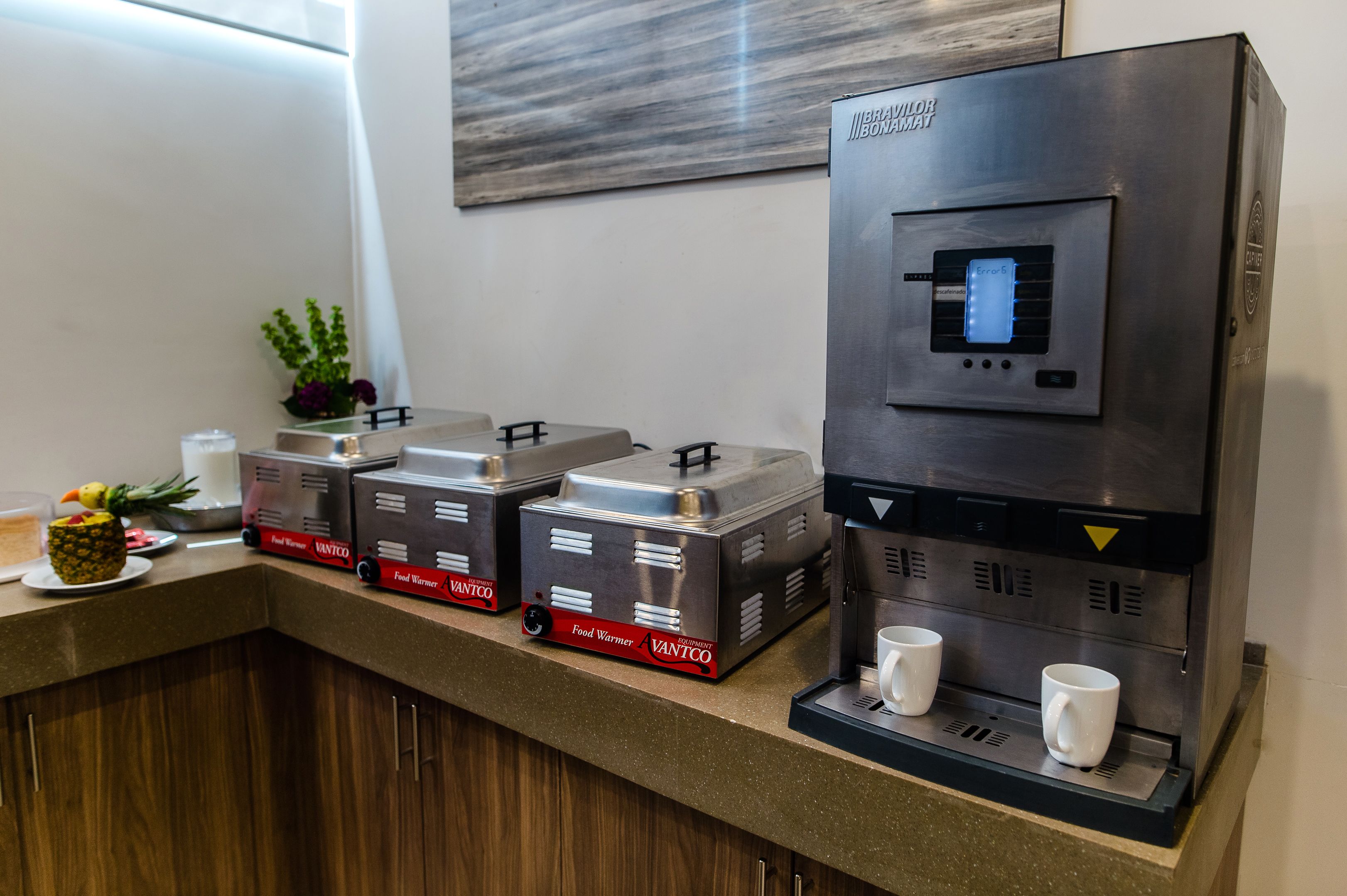 Una estación de café con una máquina de café con marca propia y dos calentadores de alimentos etiquetados como "VANTCO".