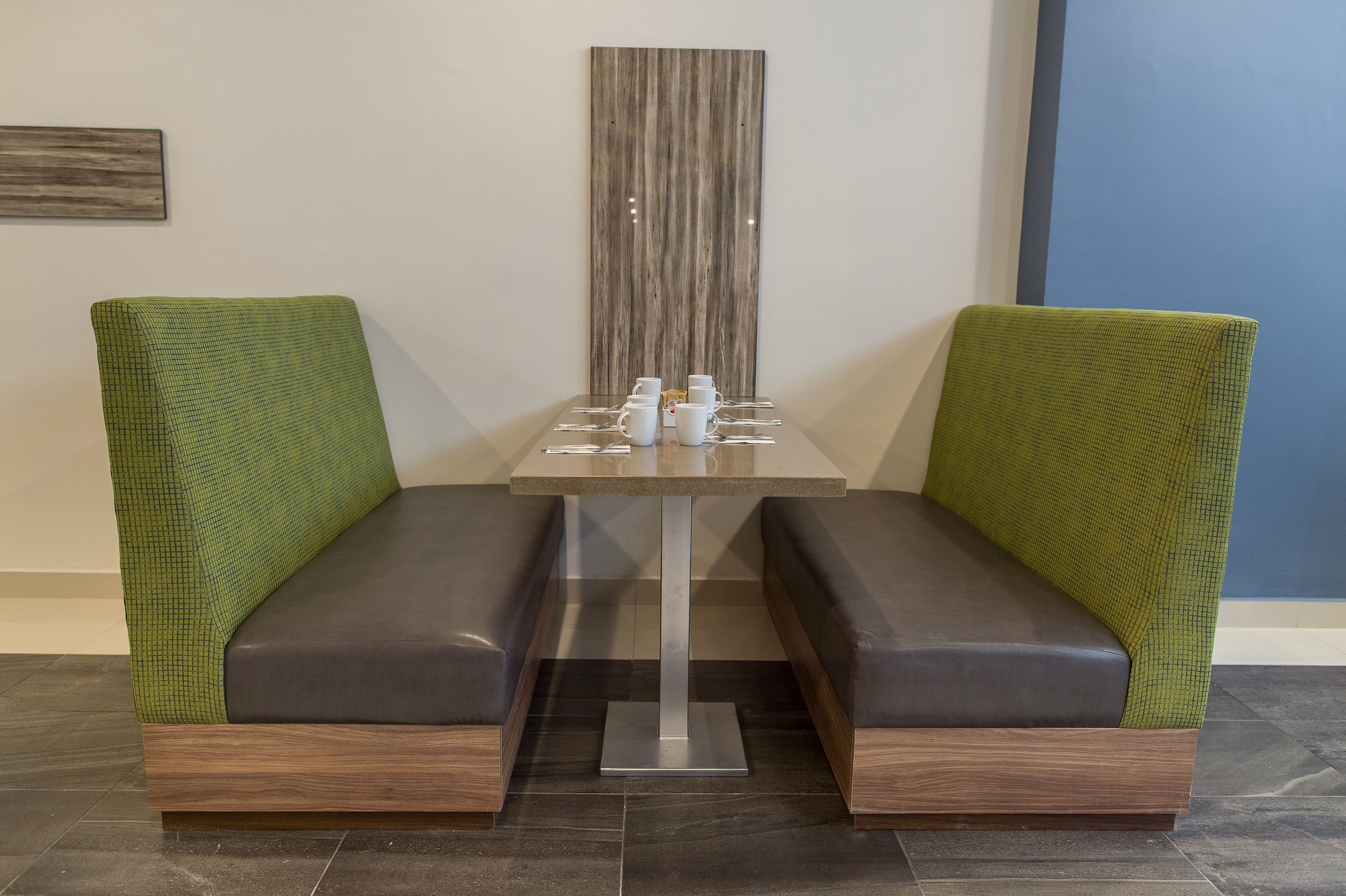 A seating area with two cushioned booths, a table with a vase and cups, and a vertical wooden panel on the wall.