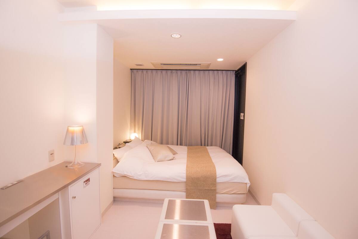 Habitación de hotel compacta con cama, mesita de noche y un pequeño rincón de descanso.