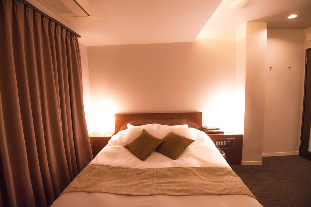 Una habitación de hotel con cama, cortinas, una mesita de noche y un atril.