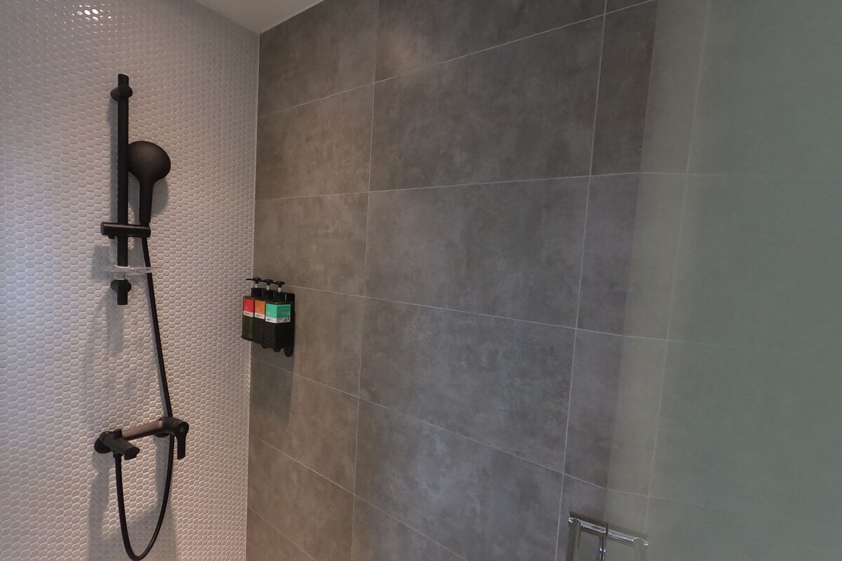 A bathroom with a shower, a towel rack, and a soap dispenser.