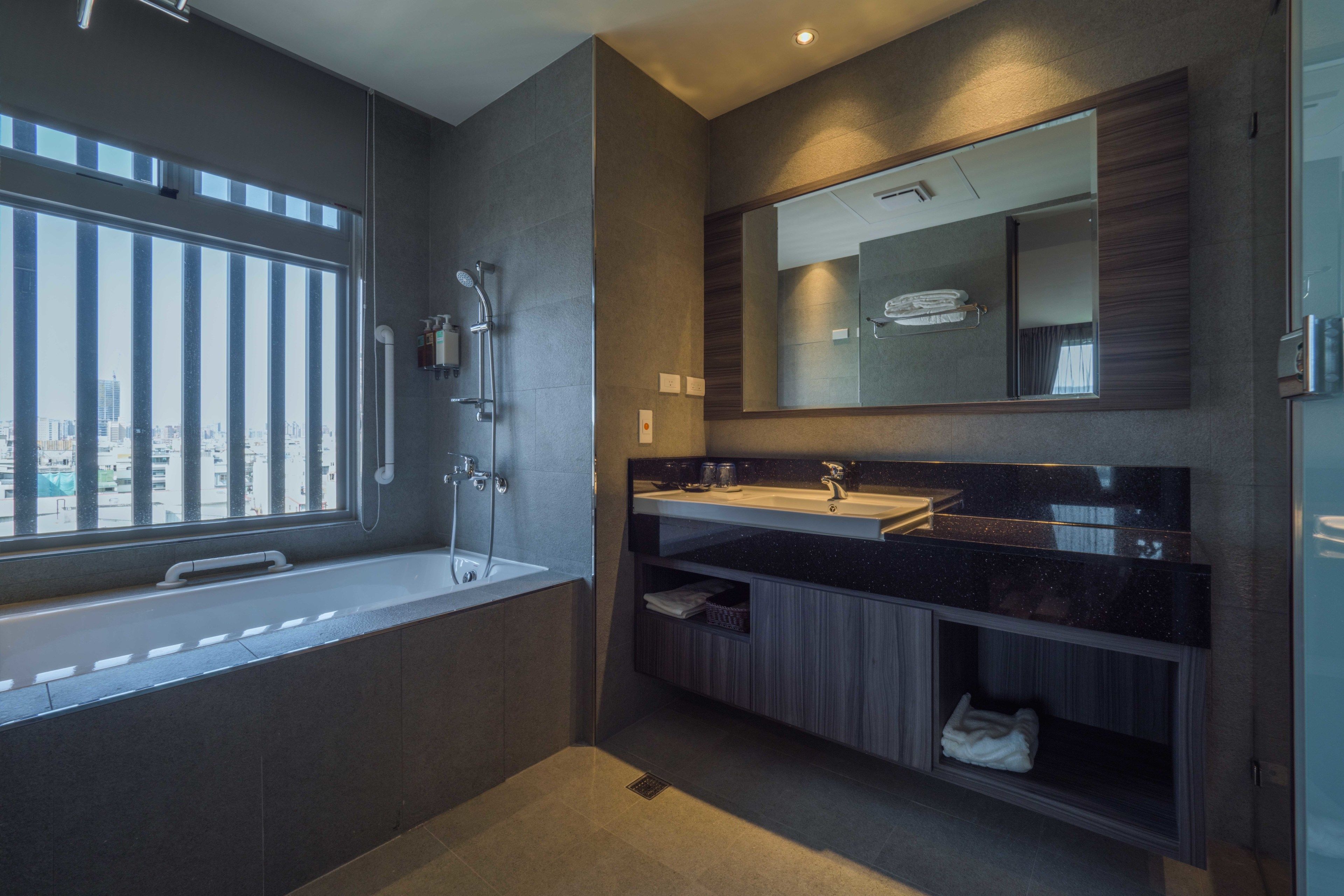 Un baño moderno con un ventanal amplio, una bañera, una ducha y un tocador con espejo.