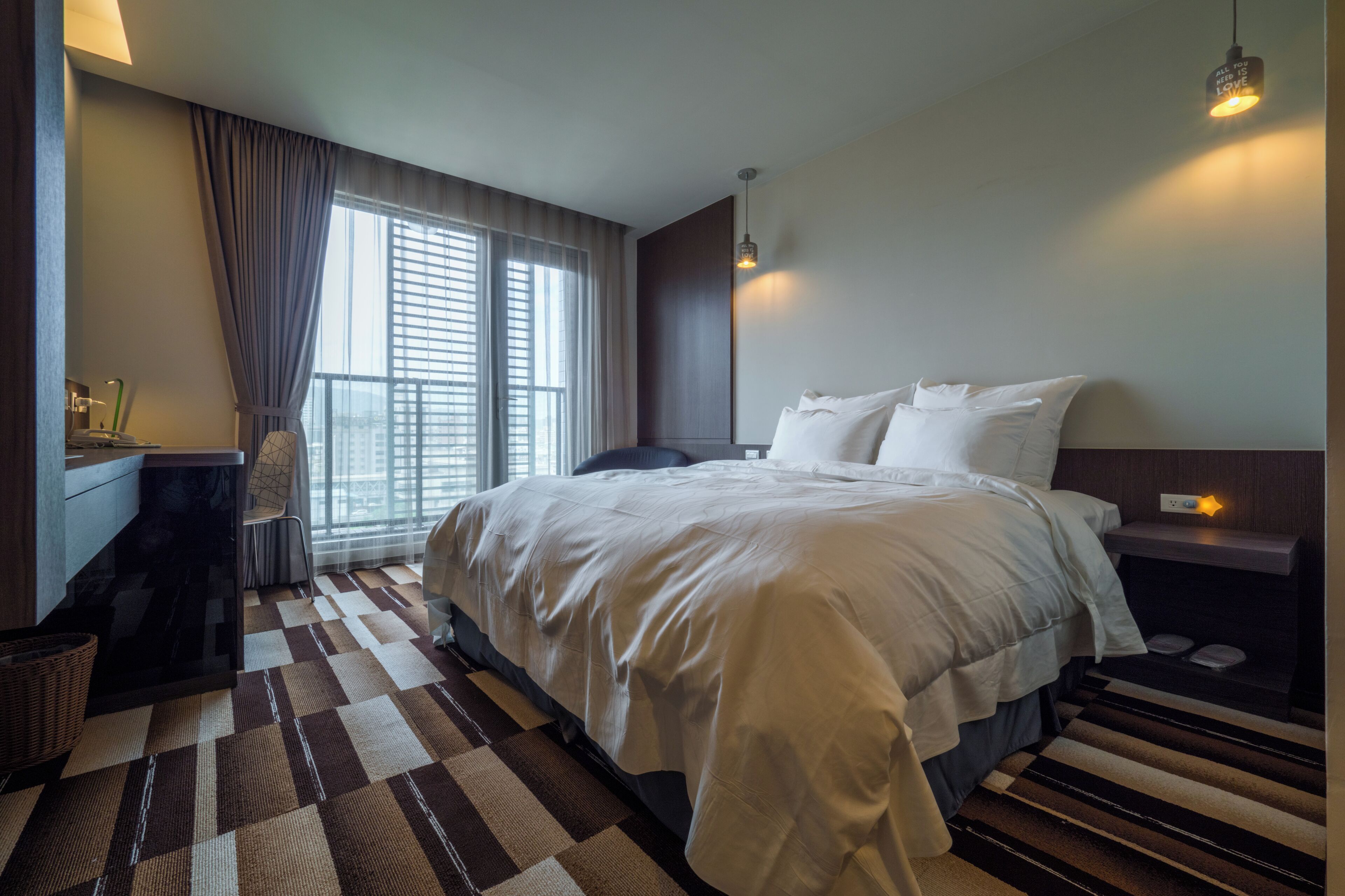A modern hotel room with a large bed, a desk, and a window with curtains.