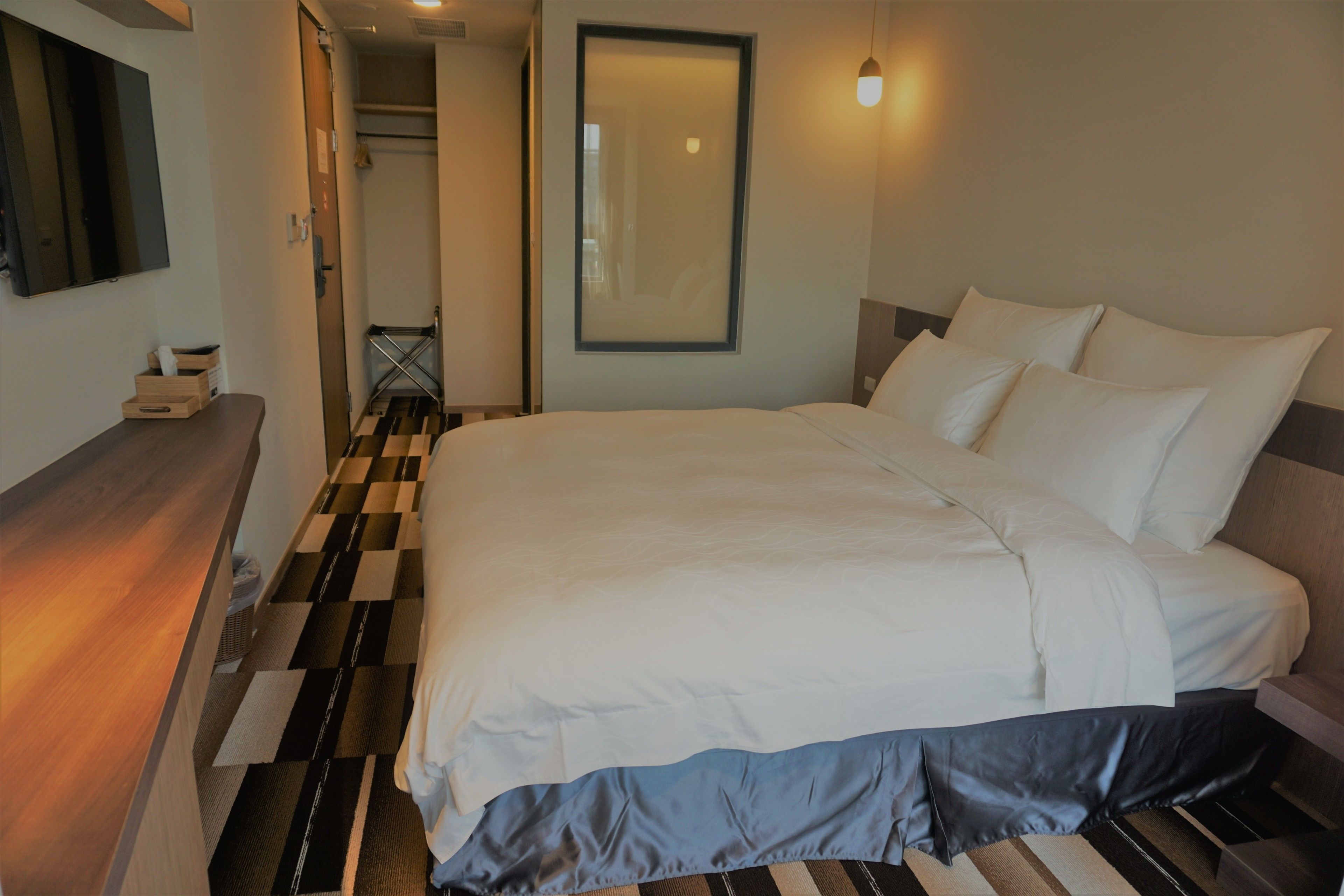 A hotel room with a large bed, a bedside table, a mirror, and a check-in counter.
