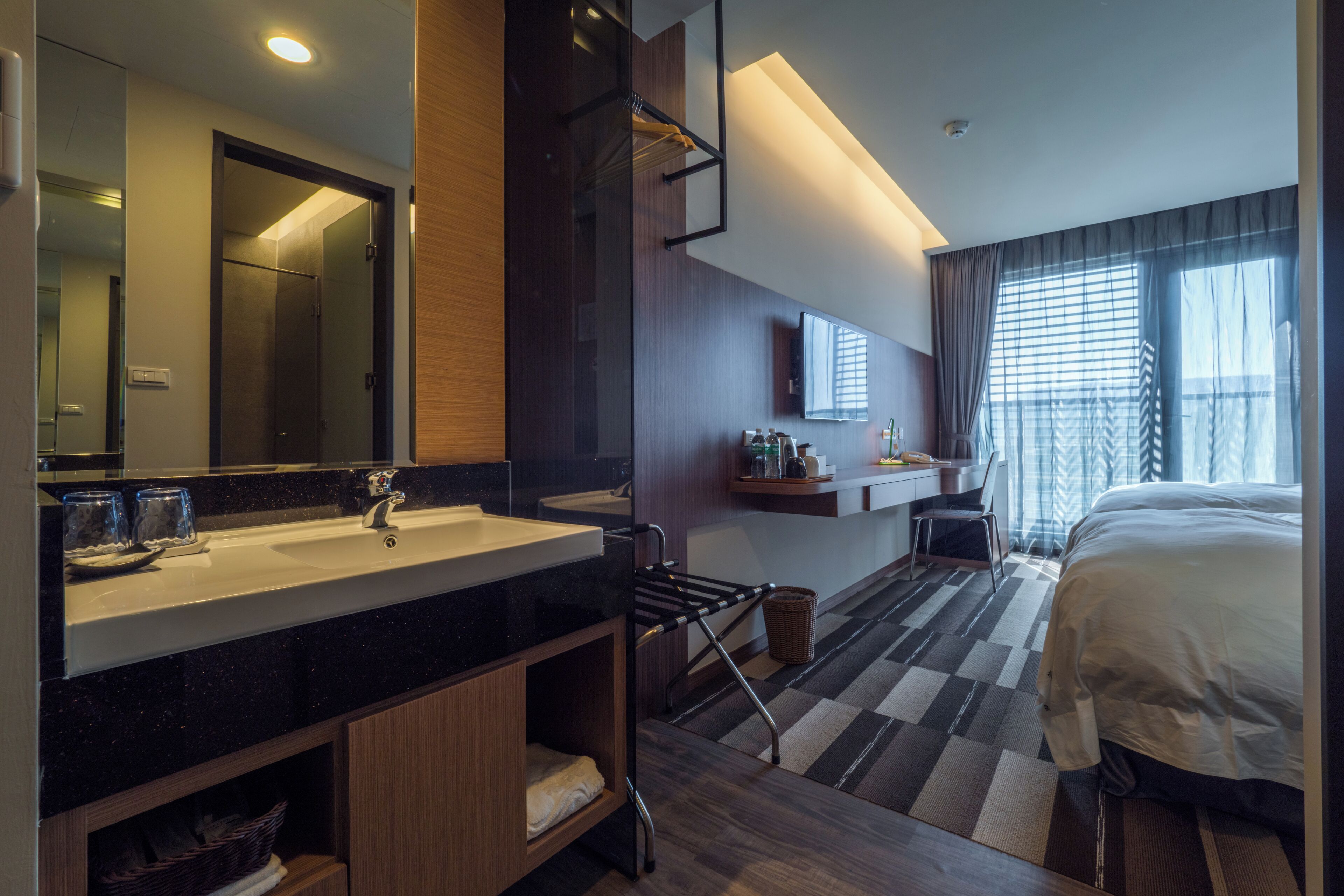 A modern hotel room with a large bed, a bathroom with a sink and mirror, and a view of the city through the window.