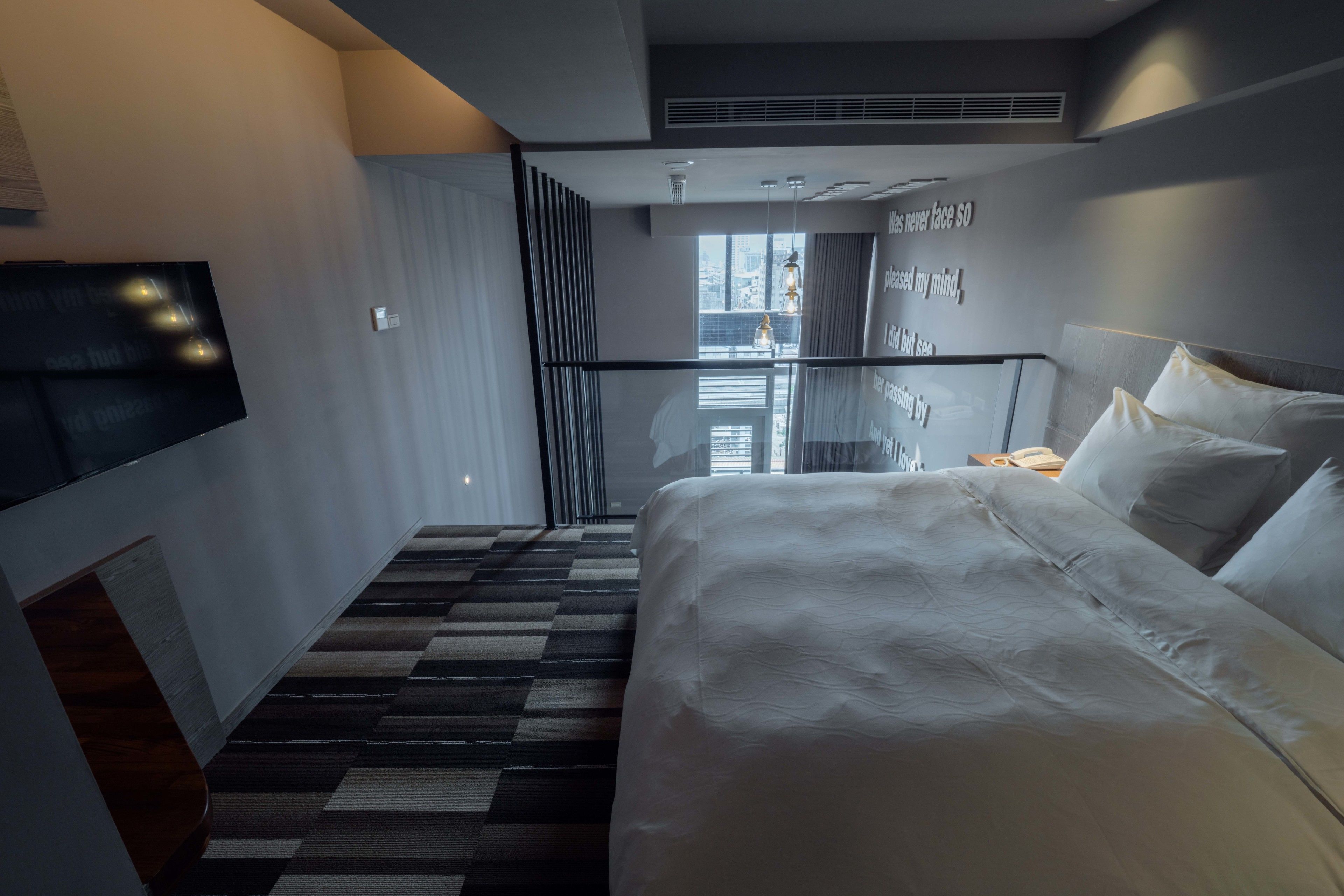 A modern hotel room with a large bed, a flat-screen TV mounted on the wall, and a staircase leading to an outdoor area.