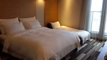 A hotel room with a large bed, a smaller bed, and a window with curtains.
