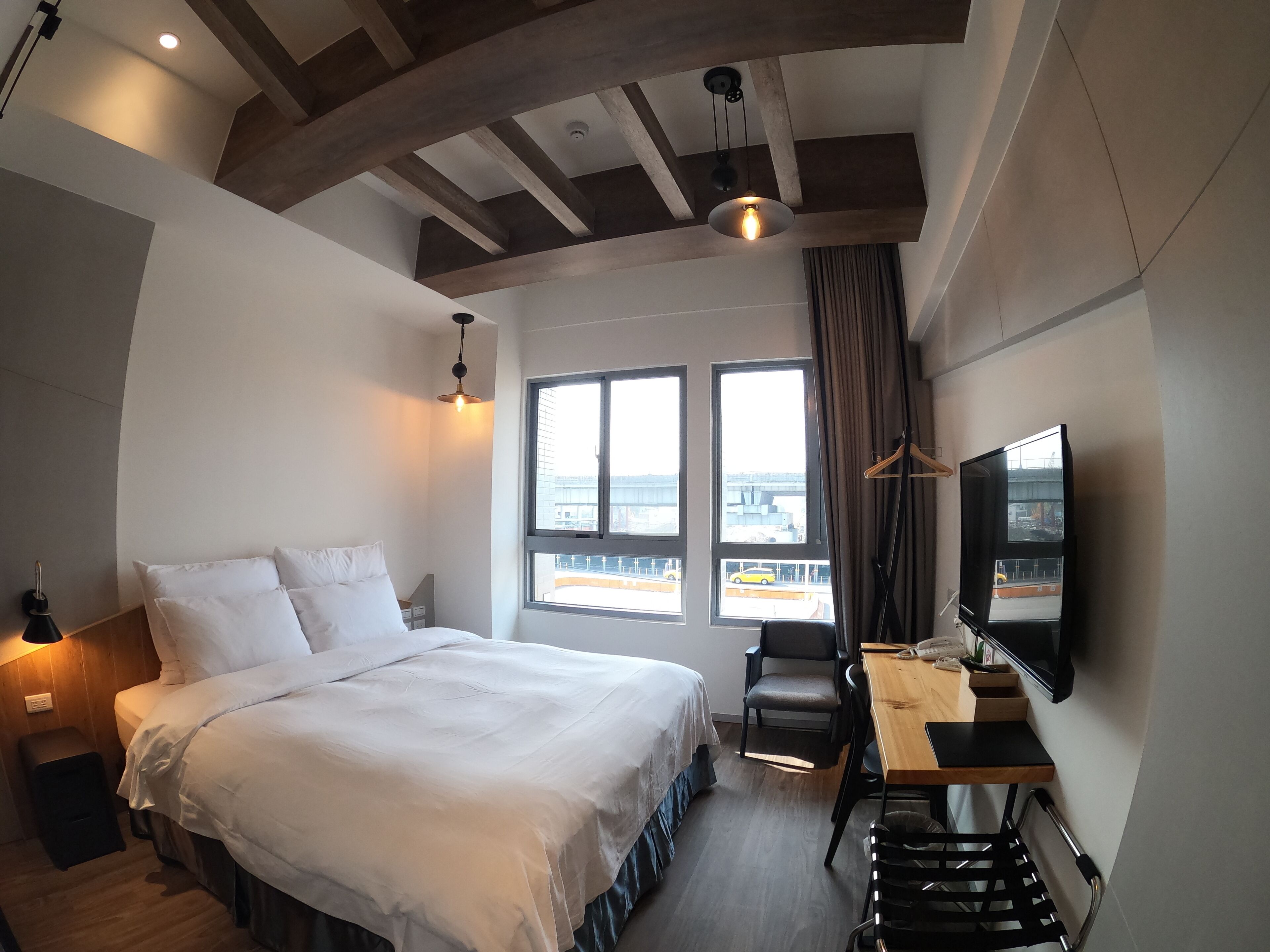 A hotel room with a bed, a desk, a chair, a TV, and large windows with a view of the city.