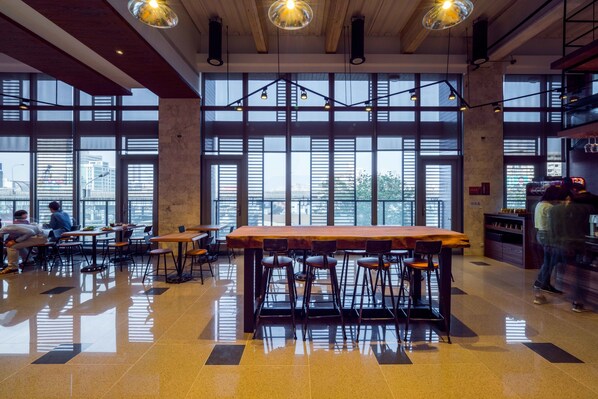 A spacious café with large windows, a long wooden table, and multiple seating areas. - Watermark Hotel Kaohsiung Station (Kaohsiung)