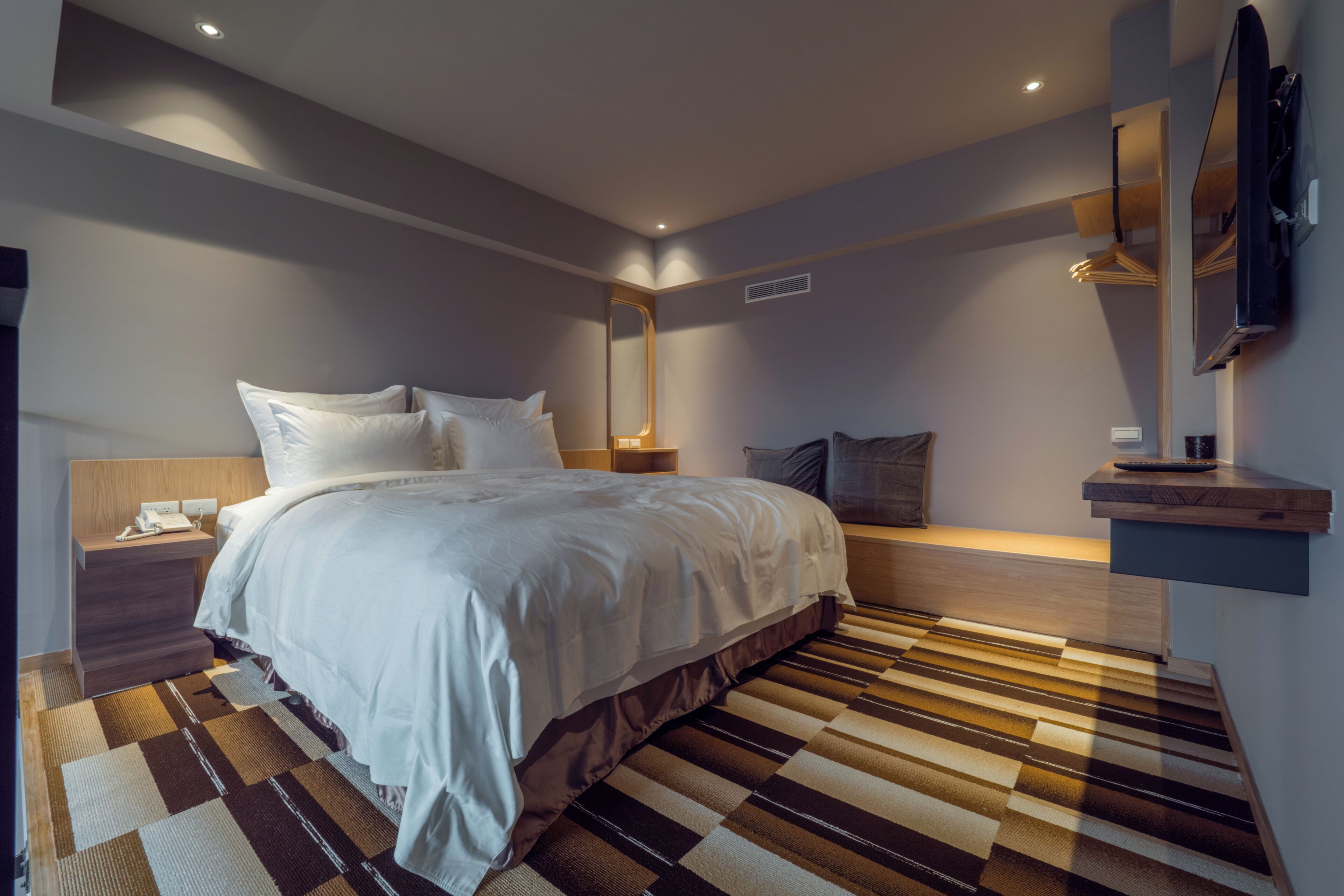 Habitación de hotel moderna con una cama grande, una mesita de noche con teléfono, un espejo y un televisor montado en la pared.