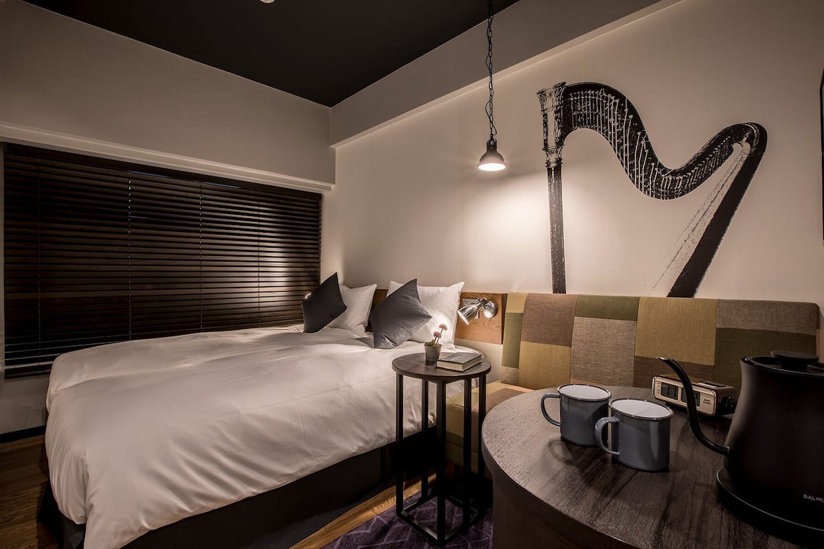 A modern hotel room with a bed, bedside table, lamp, and a wall art piece.