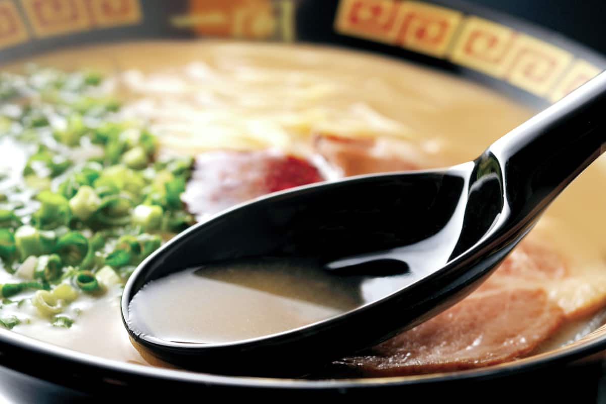 A bowl of soup with a spoon, garnished with green onions.