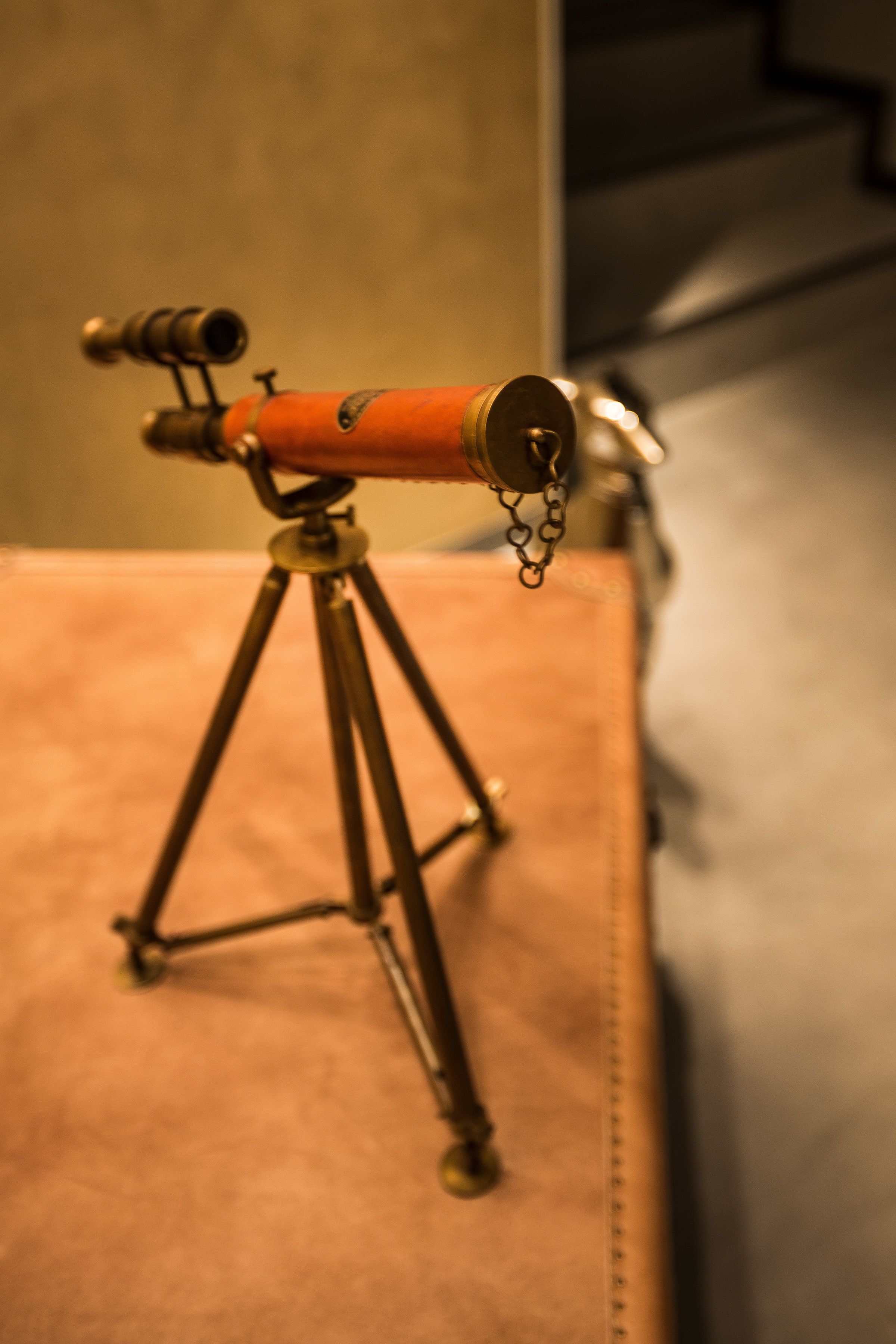 A brass telescope on a tripod, placed on a brown surface.