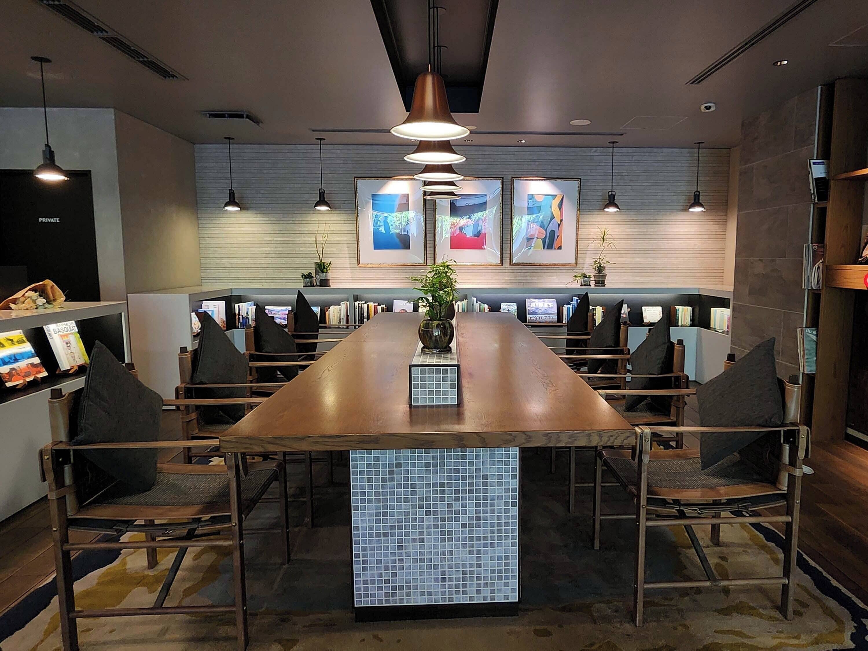 A conference room with a long table, chairs, pendant lights, framed artwork, and a tiled accent piece.