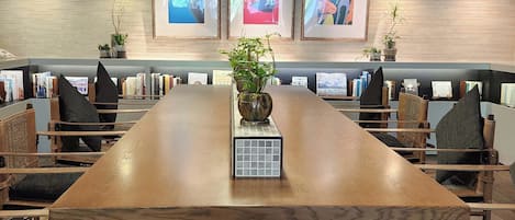 A long wooden table with chairs, framed artwork on the wall, and potted plants.