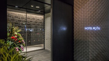 Exterior del Hotel Resol, con un diseño moderno, que presenta una pared texturizada y una entrada de vidrio transparente.