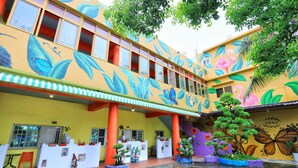 Un edificio colorido con un mural de mariposas y flores, un espacio al aire libre cubierto con plantas y una escalera que lleva a un nivel superior.