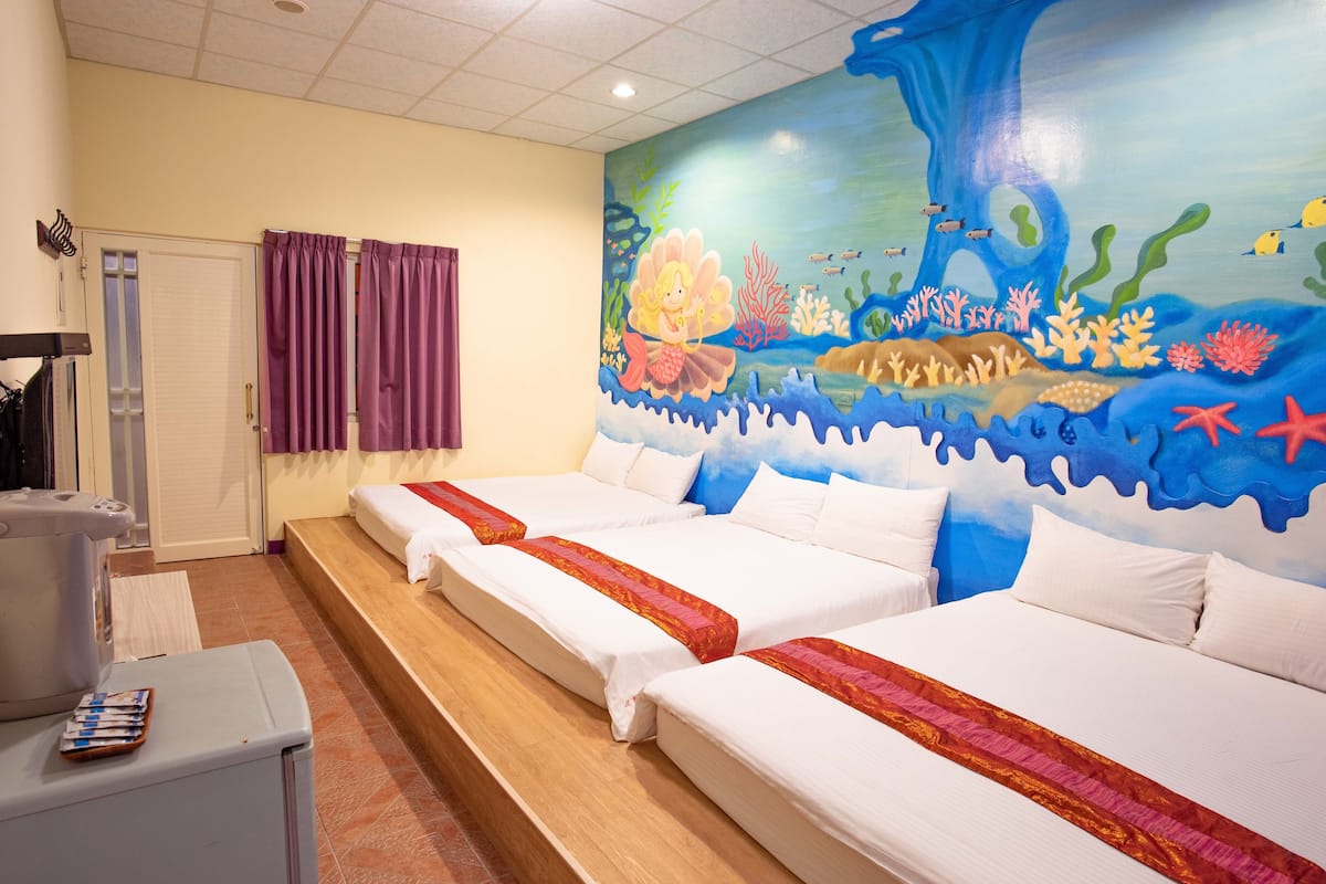 A hotel room with three beds, a bathroom, and a mural of an underwater scene.