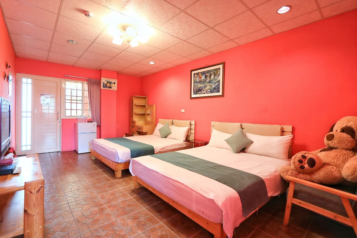 A room with two beds, a desk, a chair, a teddy bear, and a door leading to a balcony.