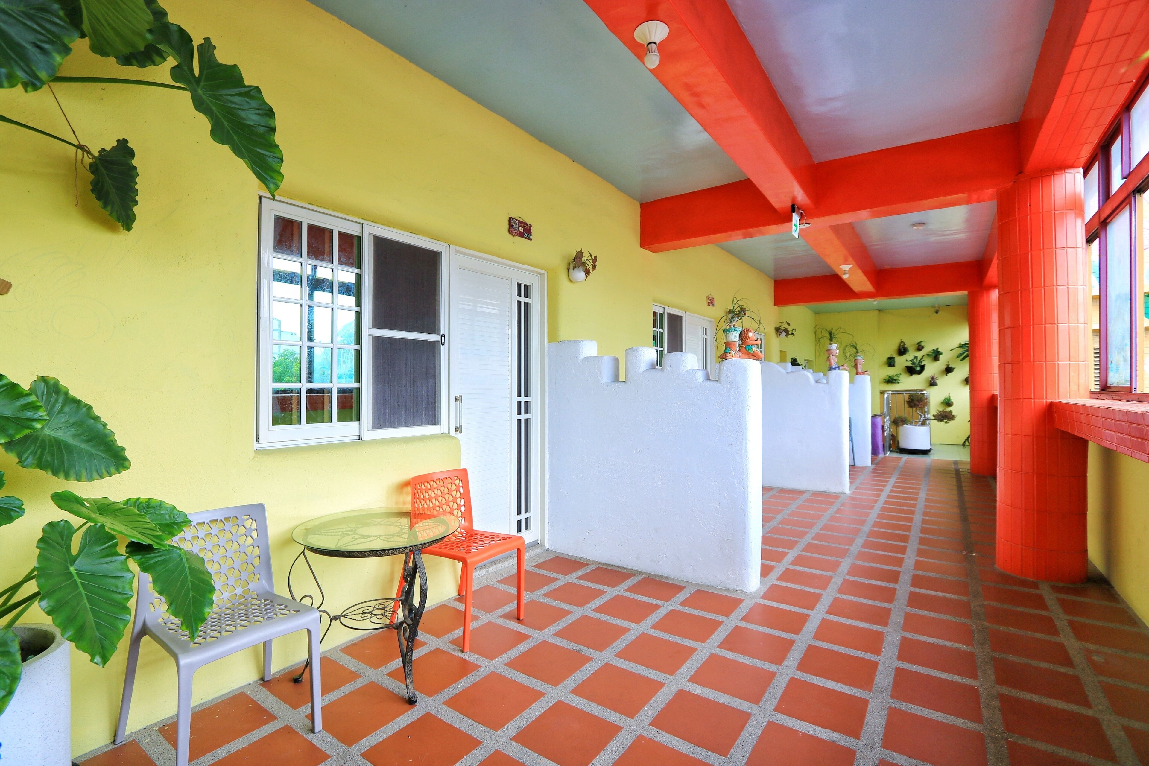 Un pasillo con pared amarilla, techo rojo y suelo de baldosas naranjas. Hay dos sillas, una mesa y una puerta blanca.