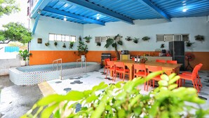 Un espacio al aire libre cubierto con piscina, mesa de comedor con sillas y plantas en macetas.