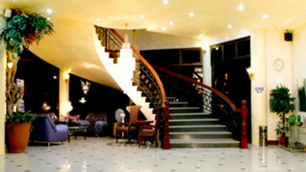A spacious lobby with a curved staircase, multiple seating areas, and potted plants. - Crown Royale Hotel (Balanga)