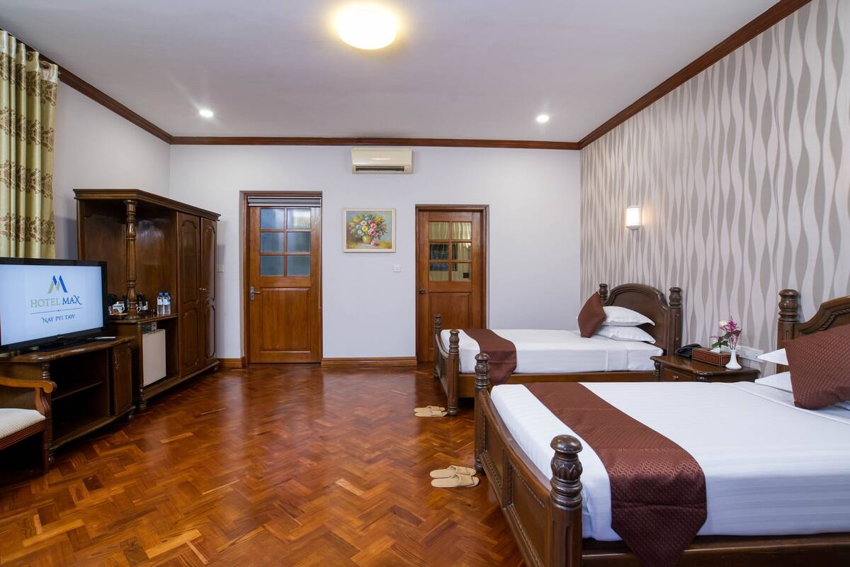 Quarto de hotel com duas camas, televisão, móveis de madeira e papel de parede estampado.