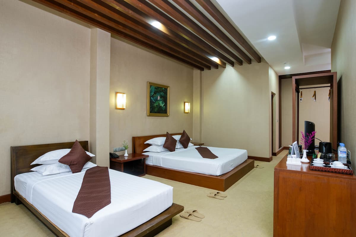 Quarto de hotel com duas camas, cabeceiras de madeira, uma escrivaninha com telefone, uma mesinha com um vaso e um quadro na parede.