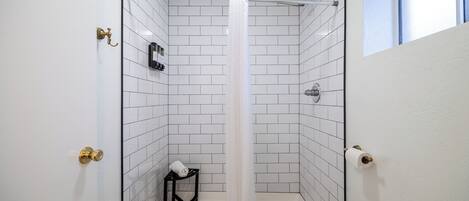 A bathroom with white tiled walls, a shower curtain, a towel on a small stool, and a toilet paper holder.