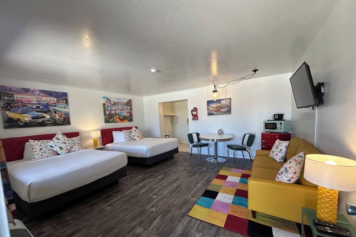 A hotel room with two beds, a sofa, a dining table, and a TV.