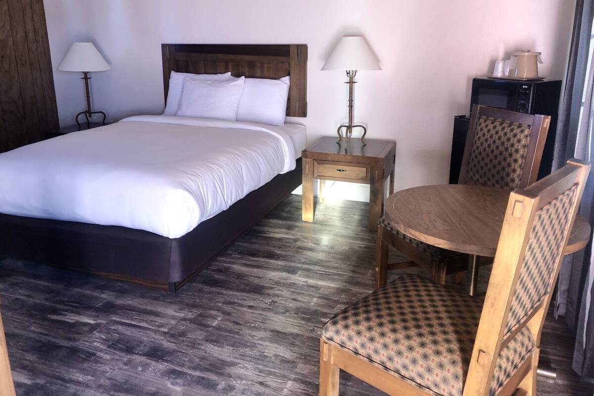 A hotel room with a large bed, two bedside tables with lamps, a wooden chair, and a small table.