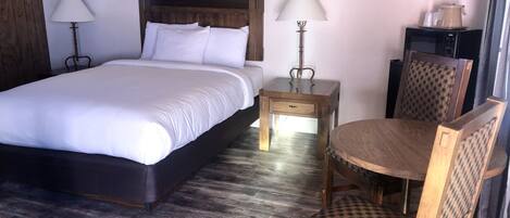 Une chambre d’hôtel avec un grand lit, deux tables de chevet avec des lampes, une chaise en bois et une petite table.
