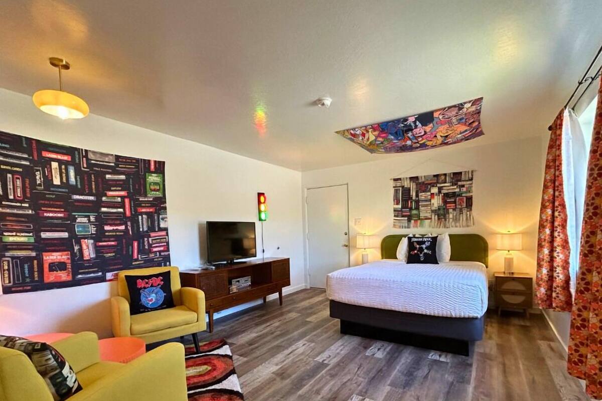 A modern hotel room with a large bed, a TV, a bookshelf, and a wall with a comic book mural.