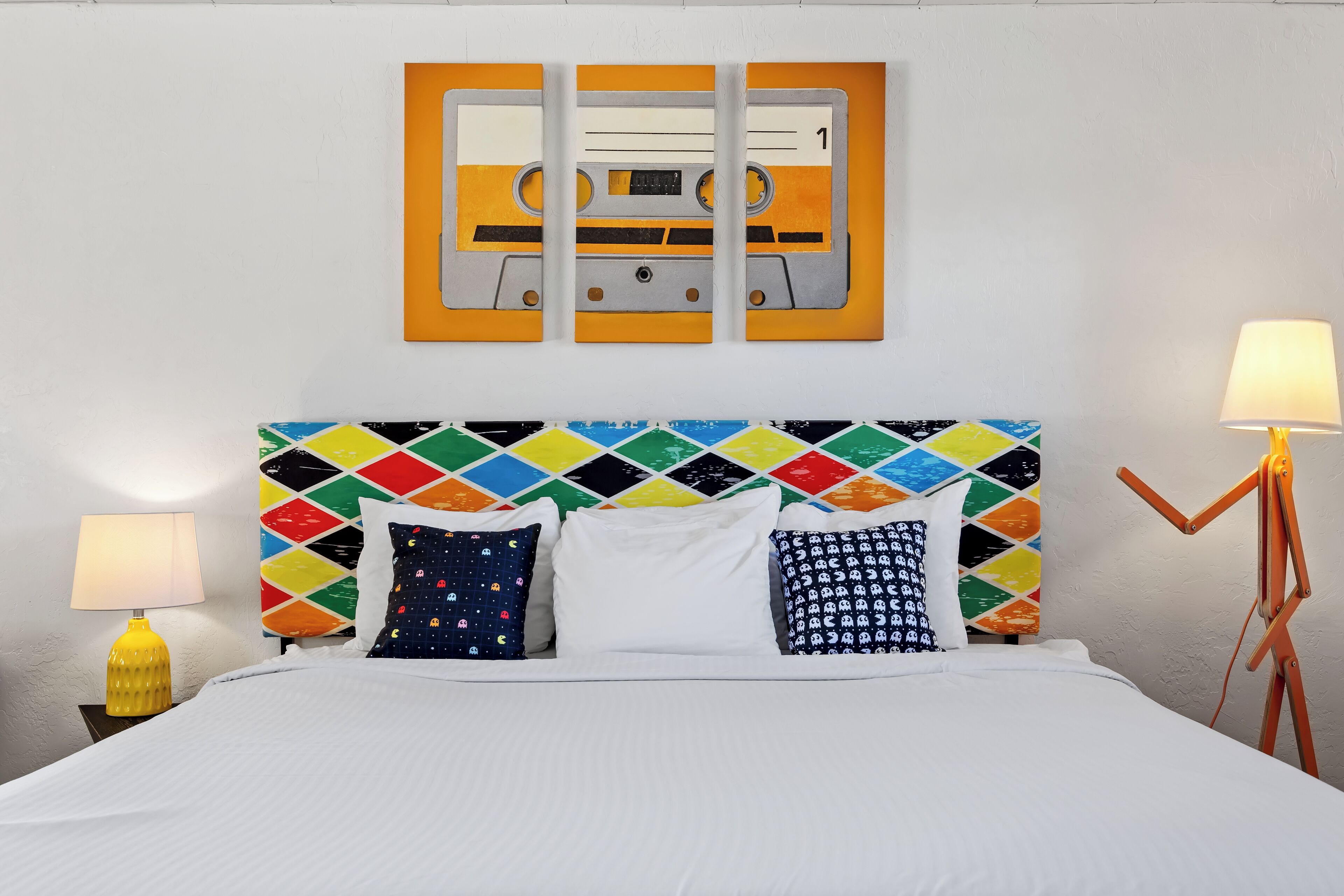 A bed with a colorful diamond-patterned headboard, white bedding, and two lamps on either side.
