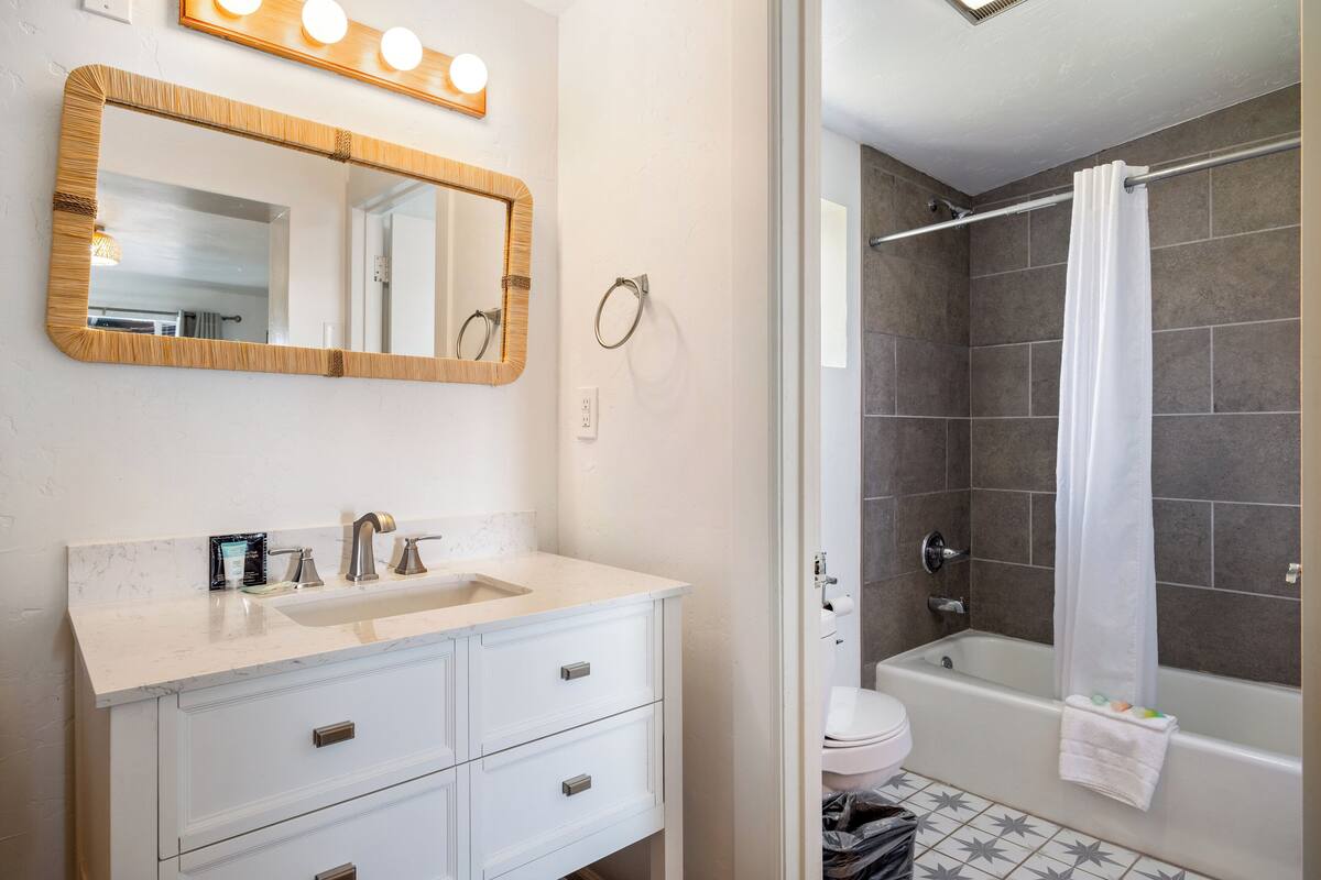 A bathroom with a white vanity, a mirror with lights, a shower with a curtain, and a toilet.