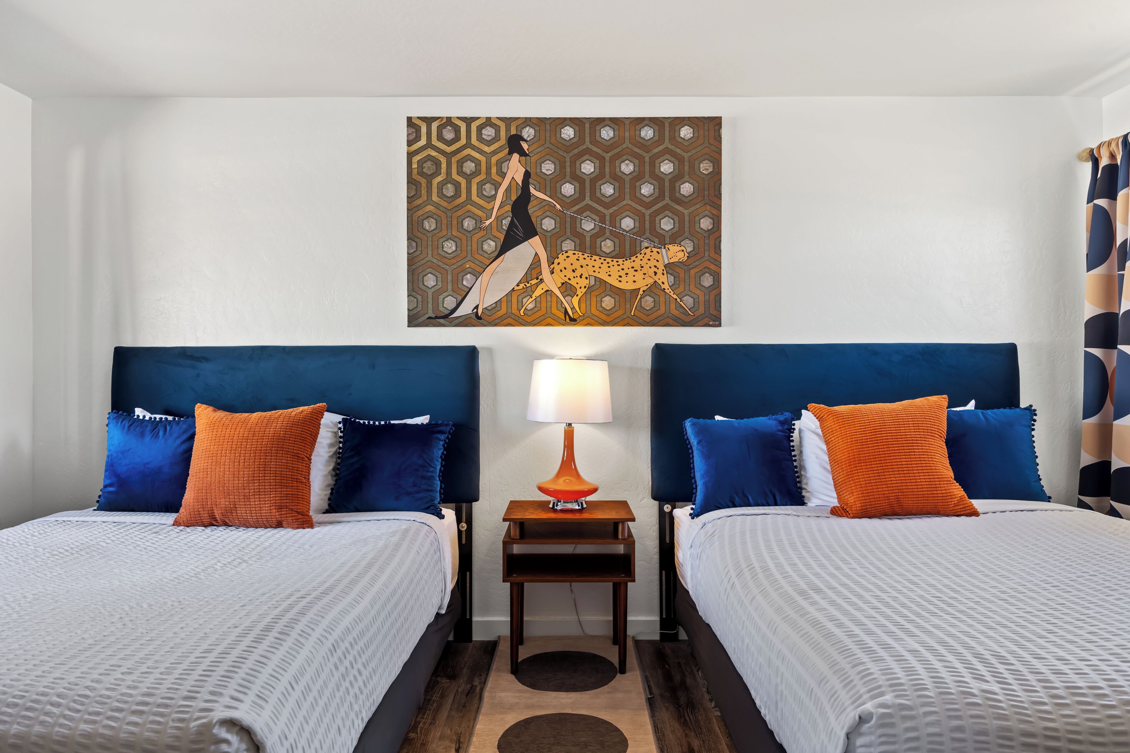 A hotel room with two beds, a nightstand with a lamp, and a painting on the wall.