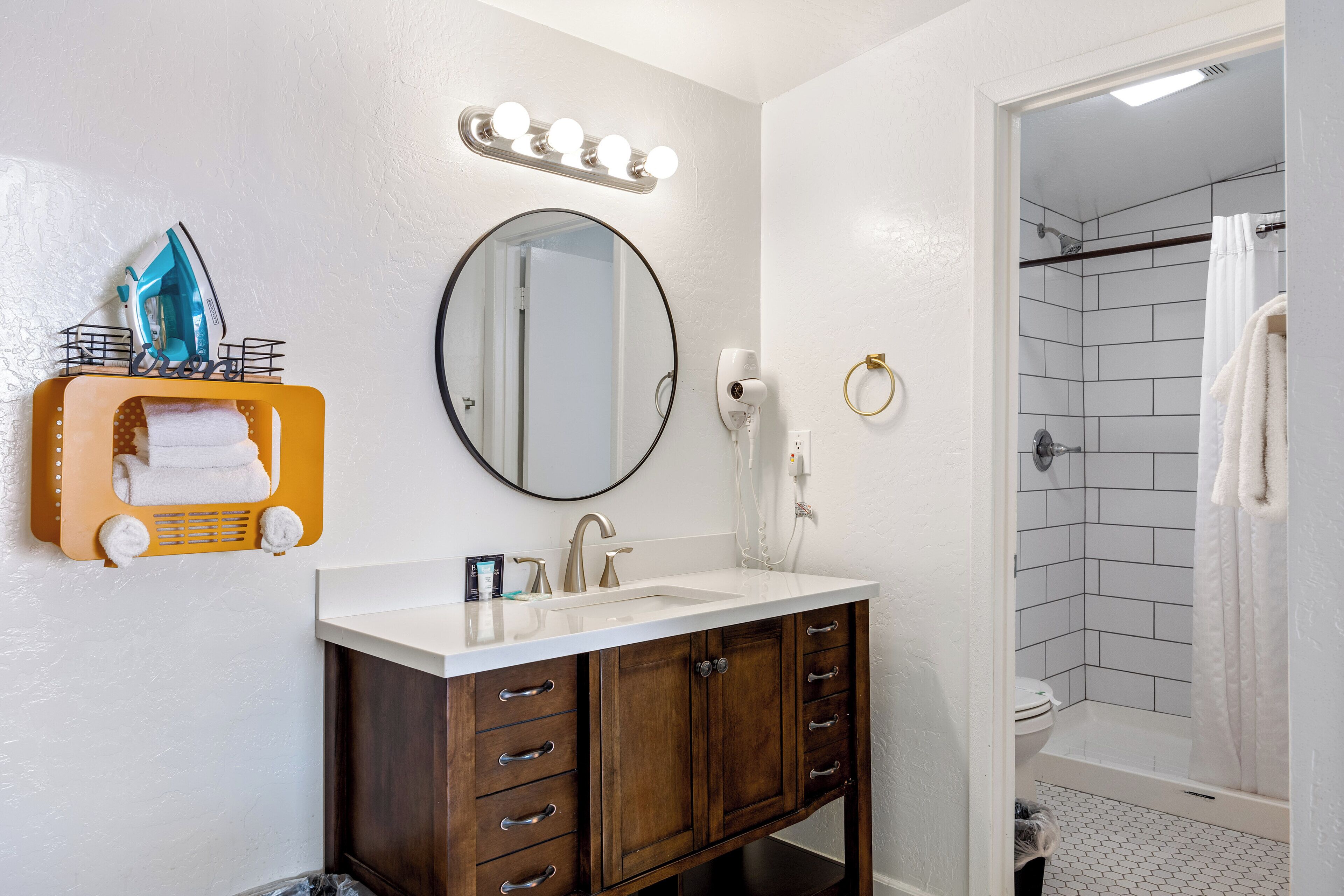 Un baño con tocador, lavabo, espejo y ducha.
