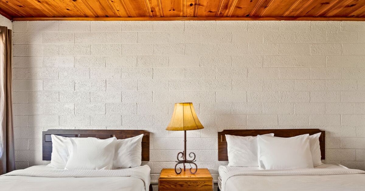 A double room with two beds, a wooden ceiling, and a brick wall.