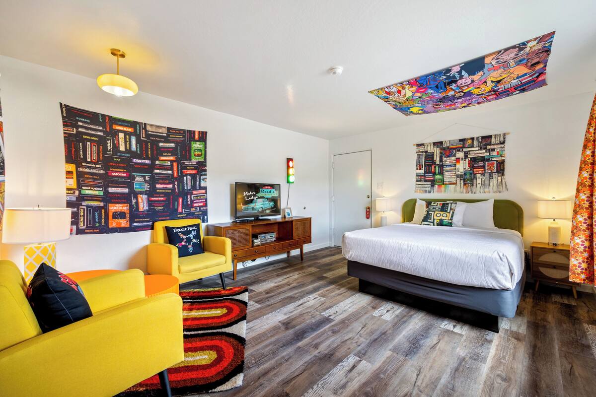 A modern hotel room with a bed, yellow armchair, and a television on a wooden dresser.
