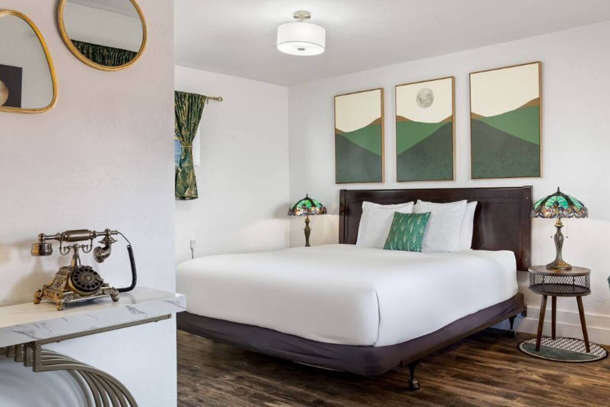 A hotel room with a large bed, a desk, two bedside tables, and artwork on the walls.
