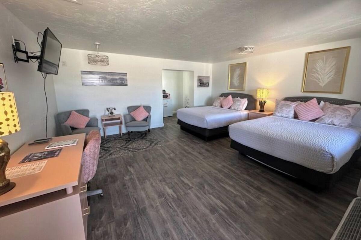 A hotel room with two beds, a desk, a chair, a TV, and artwork on the walls.
